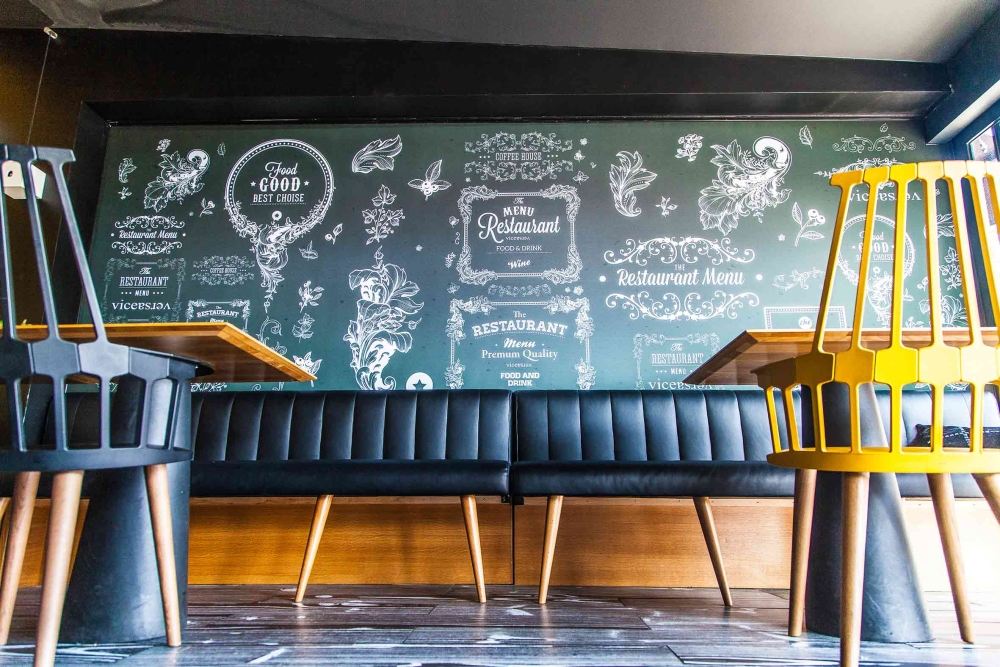 Salle de restaurant moderne avec banquette noire, chaises jaunes et mur ardoise design